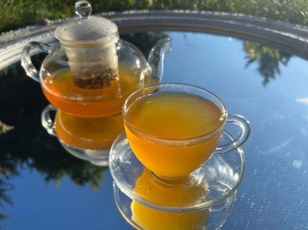 Spice and Roots Herbal Tea Blend Warm lifestyle photo of a glass teapot pouring golden herbal TEATOX tea into a clear cup, highlighting the vibrant hue from turmeric and ginger roots.