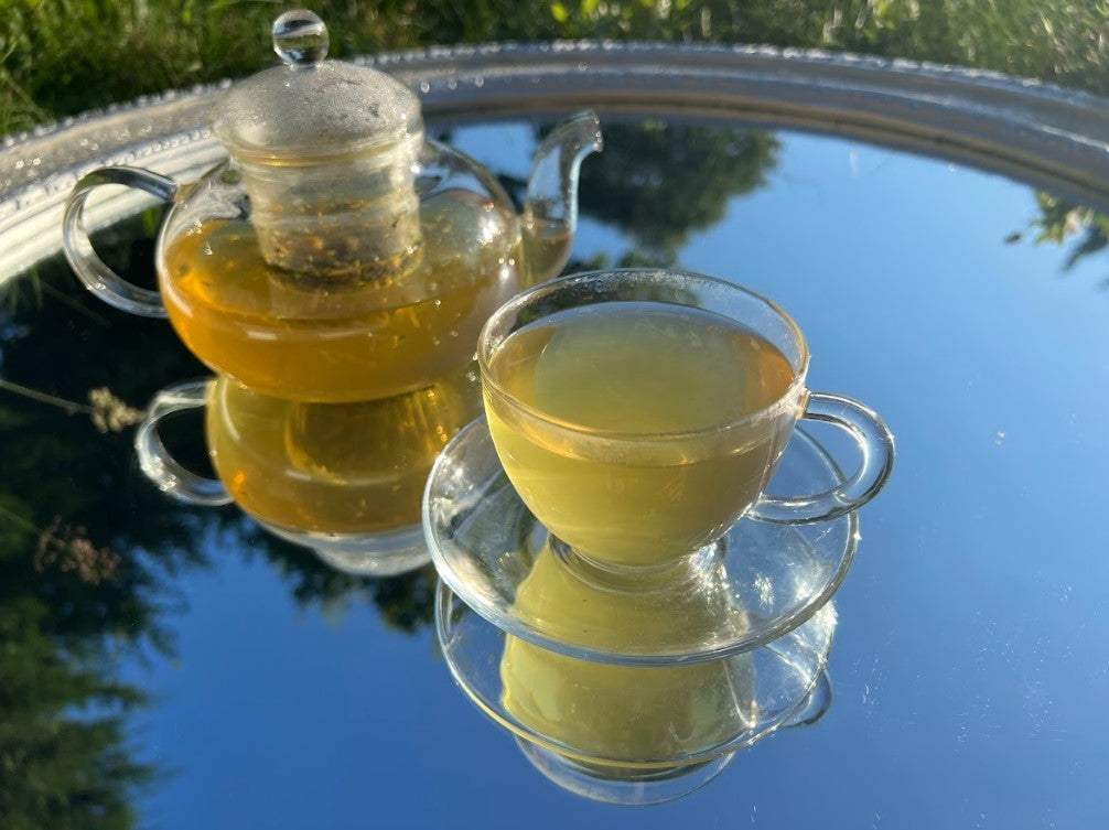 TUMMY TEA Soother Herbal Blend Lifestyle photo of a teapot and cup filled with warm, golden-brown TUMMY TEA, showcasing a comforting herbal infusion with earthy green yellow tones from roots, petals, and spices.
